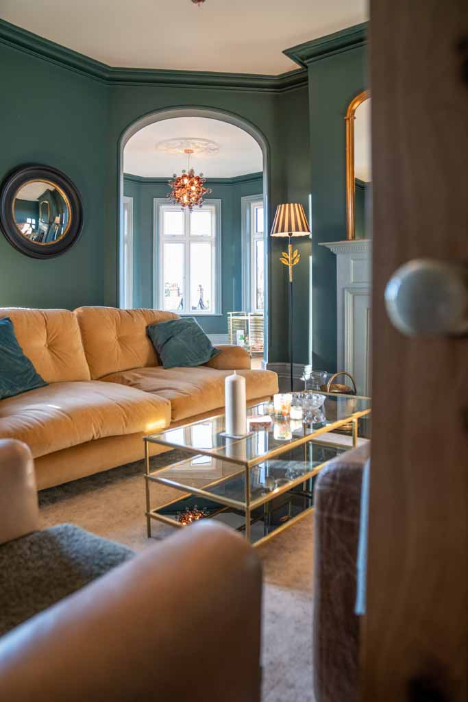 Staircase with wooden steps and glass balustrade, leading to an upper floor. The area is well-lit by natural light from a large window, giving a modern and airy feel.